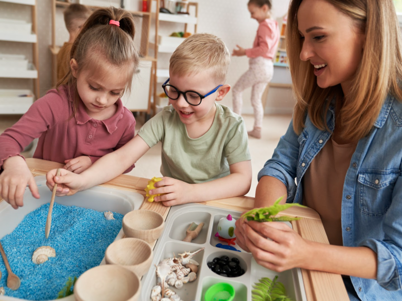 Erzieherung beschäftigt sich mit einem Jungen und einem Mädchen mit einem Experiementierkastenin einem Kindergarten